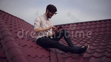 年轻开朗<strong>的</strong>嬉皮士坐在屋顶上，手里拿着智能手机，戴着<strong>圆圆的</strong>太阳镜和衬衫。